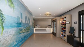 Zona de recepción con diseño moderno, que incluye un mostrador de recepción, una pared con un mural de paisaje urbano y una exhibición de aperitivos.