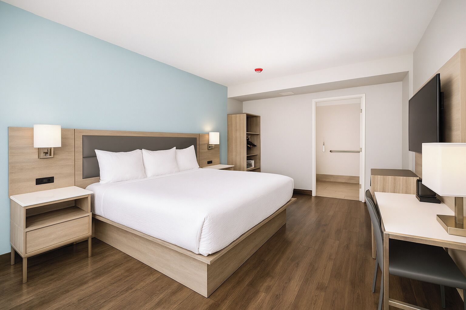 A modern hotel room with a large bed, bedside tables, a desk, and a TV.