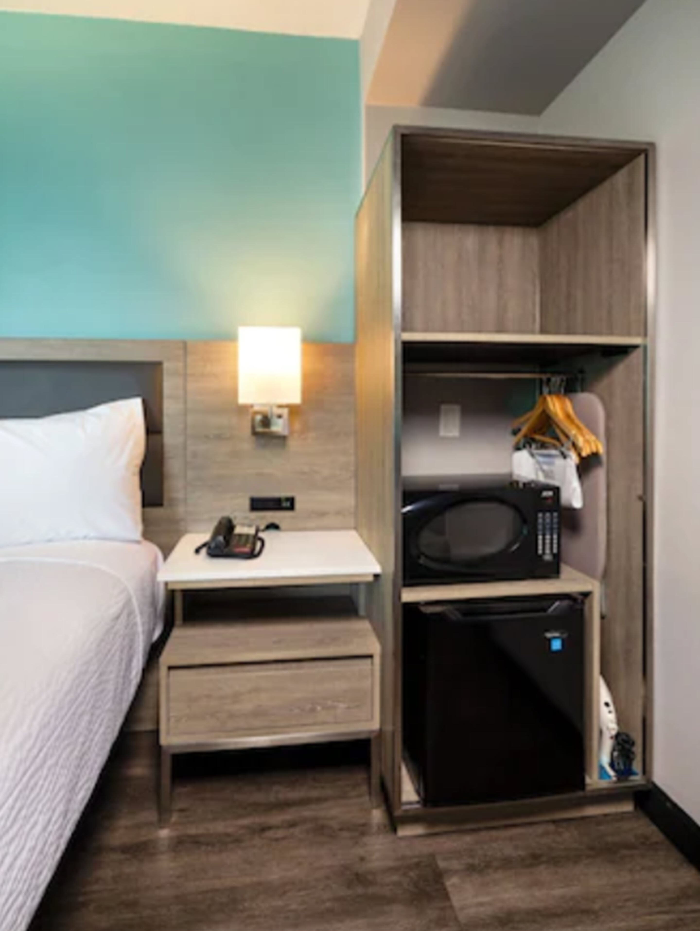 Une chambre d’hôtel comprenant un lit, une table de chevet, une lampe et un placard intégré avec un four à micro-ondes et un petit appareil électroménager.