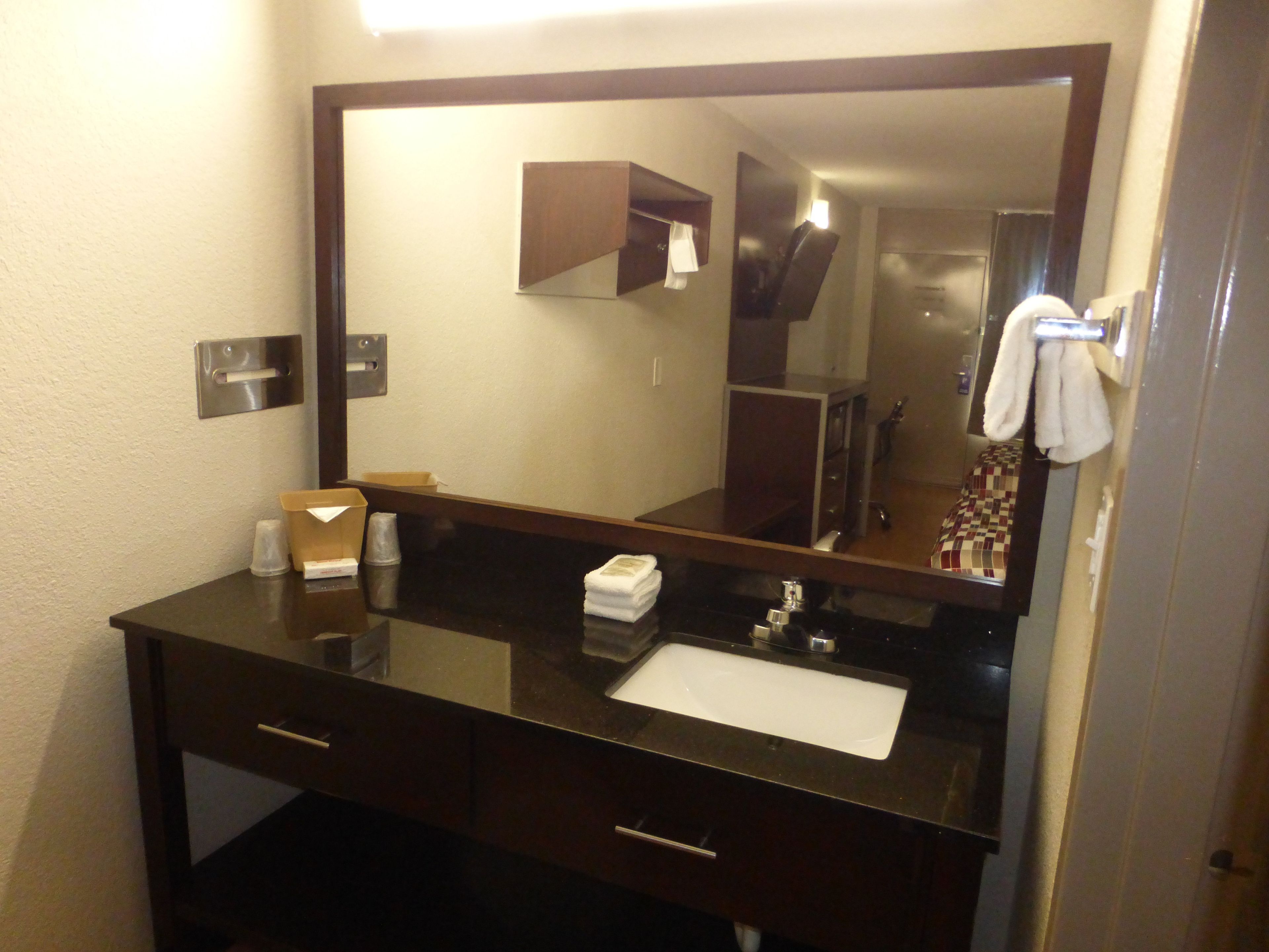 A hotel bathroom with a dark vanity, a mirror, a sink, and a towel rack.
