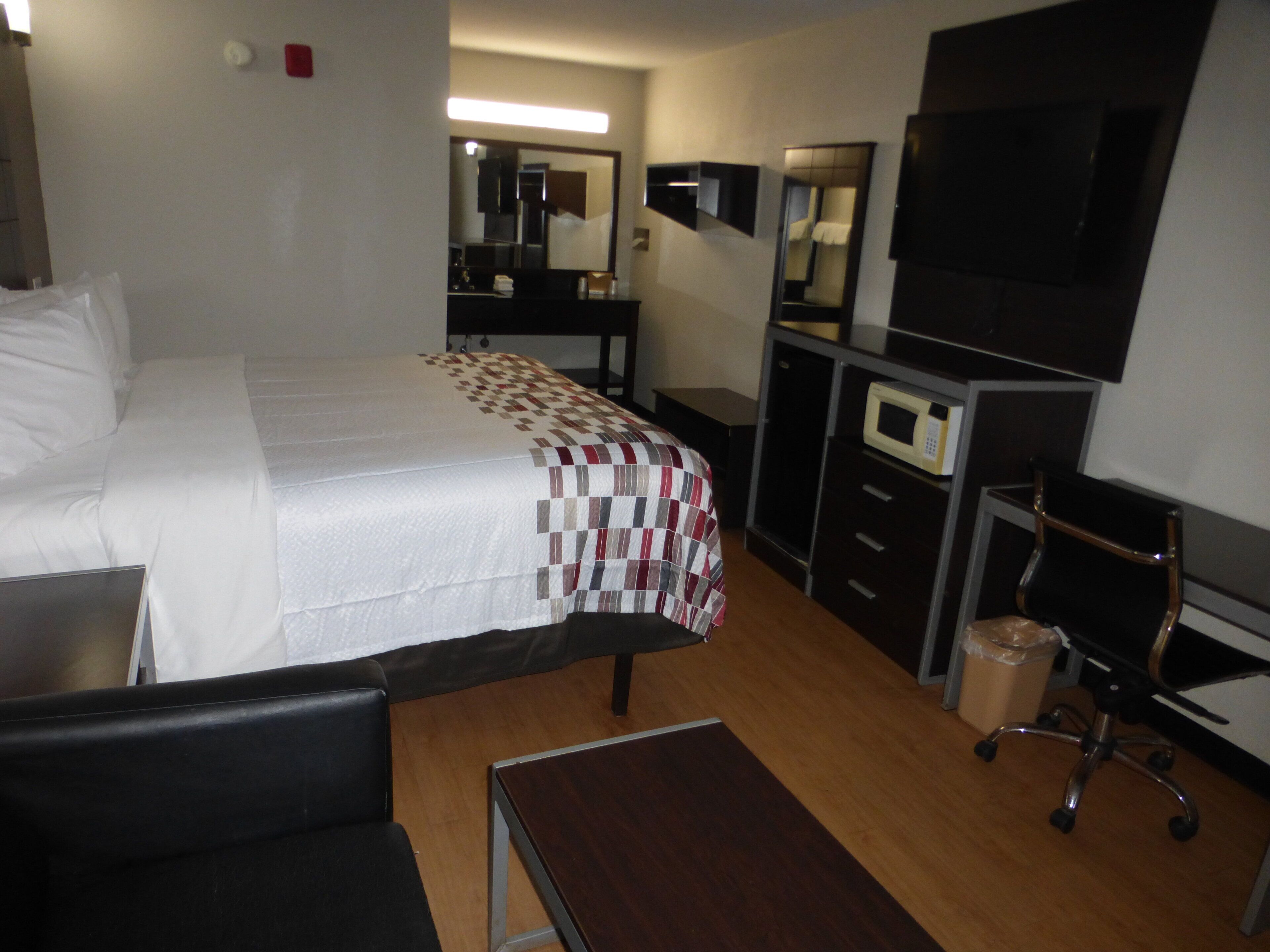 Een hotelkamer met een bed, een bureau, een stoel, een televisie, een magnetron en een spiegel.