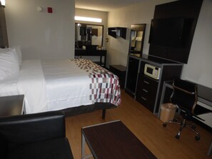 A hotel room with a bed, a desk, a chair, a TV, a microwave, and a mirror.