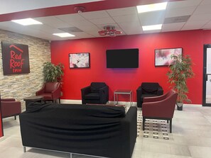 Zona de recepción de Red Roof Inn con una pared roja, dos plantas en macetas, un sofá negro y un televisor de pantalla plana.