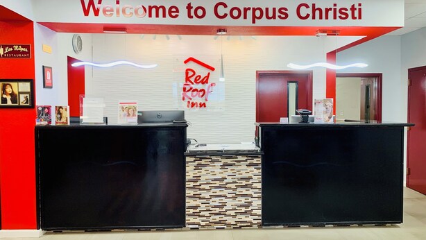 Un área de recepción con un letrero que dice 'Welcome to Corpus Christi', el logotipo de Red Roof Inn y un mostrador de recepción.