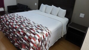 Una habitación de hotel con una cama grande, cabecera, mesita de noche, una silla y una pequeña mesa.