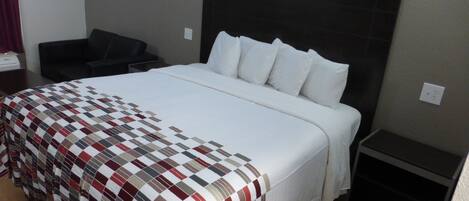 Una habitación de hotel con una cama grande, cabecera, mesita de noche, una silla y una pequeña mesa.
