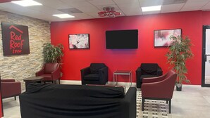 Zona de recepción de Red Roof Inn con una pared roja, dos plantas en macetas, un sofá negro y un televisor de pantalla plana.