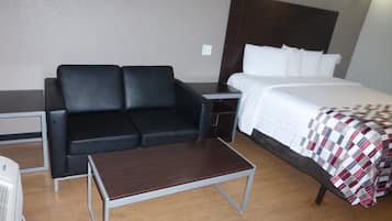 Habitación de hotel con una cama, un sofá de cuero negro, una mesita pequeña y una mesita de noche.