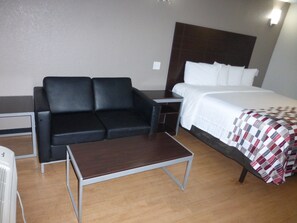 Habitación de hotel con una cama, un sofá de cuero negro, una mesita pequeña y una mesita de noche.