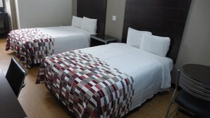 A hotel room with two beds, each with a checkered bedspread, a nightstand, a chair, and a small table. - Red Roof Inn Corpus Christi North - Near Downtown (Corpus Christi)