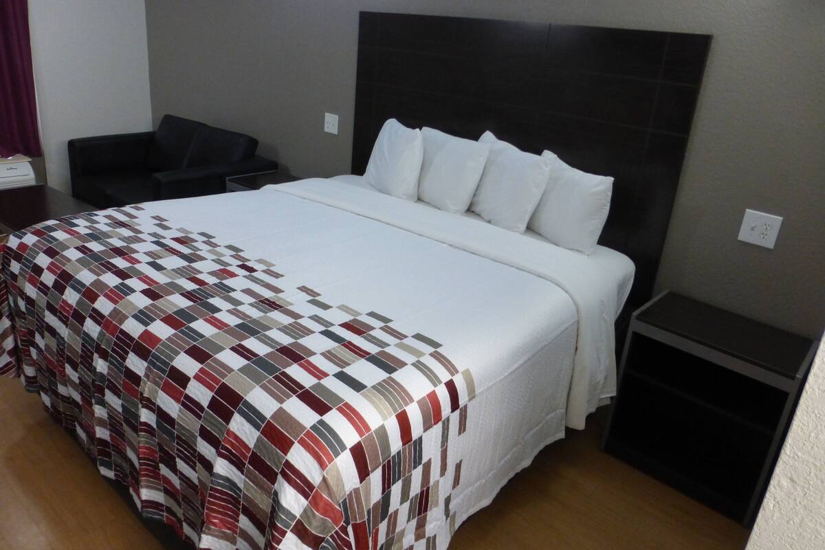 Une chambre d’hôtel avec un grand lit, une tête de lit, une table de chevet, une chaise et une petite table.