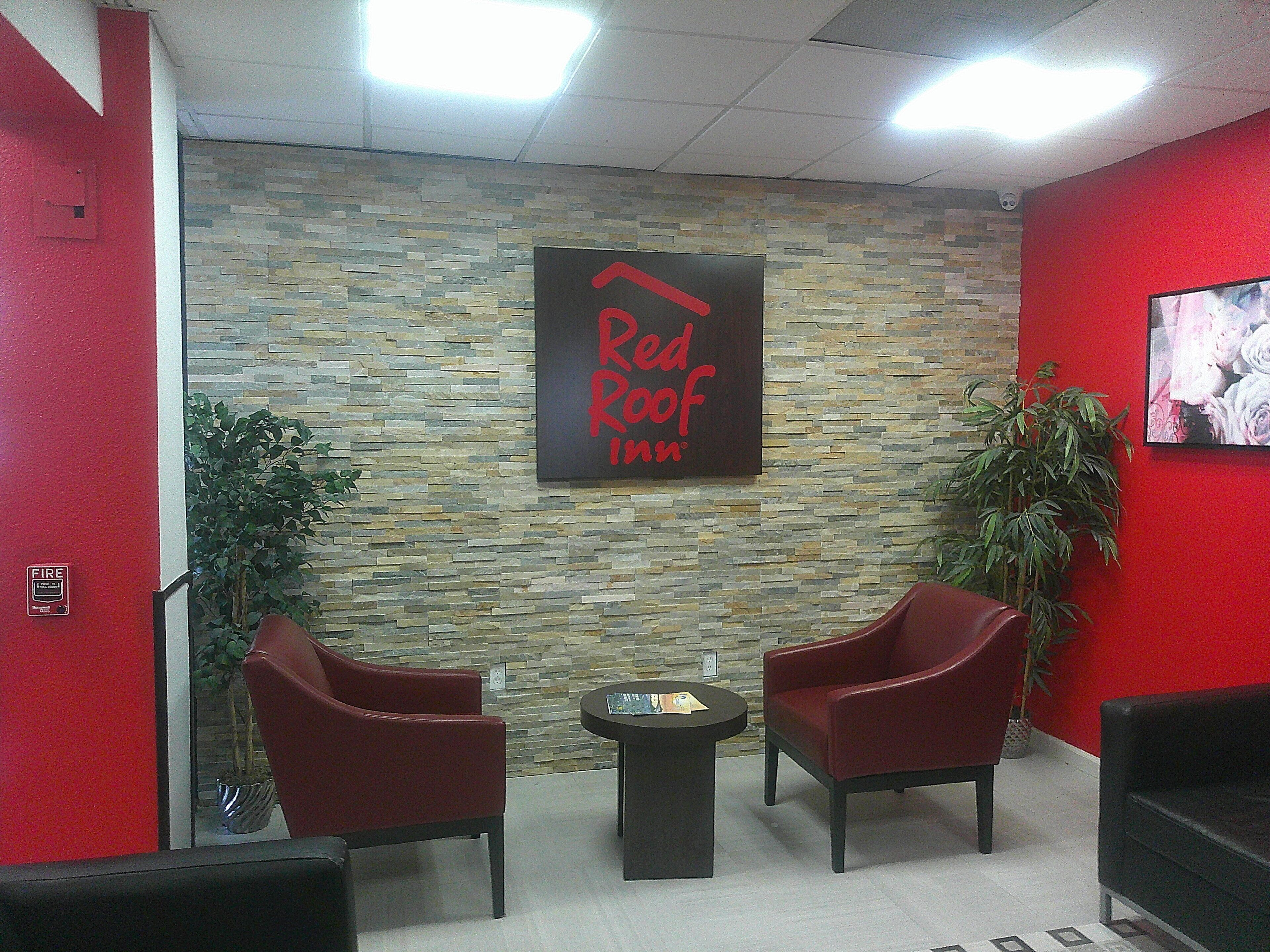 A Red Roof Inn lobby with a stone wall, two red chairs, a small table, and a potted plant.
