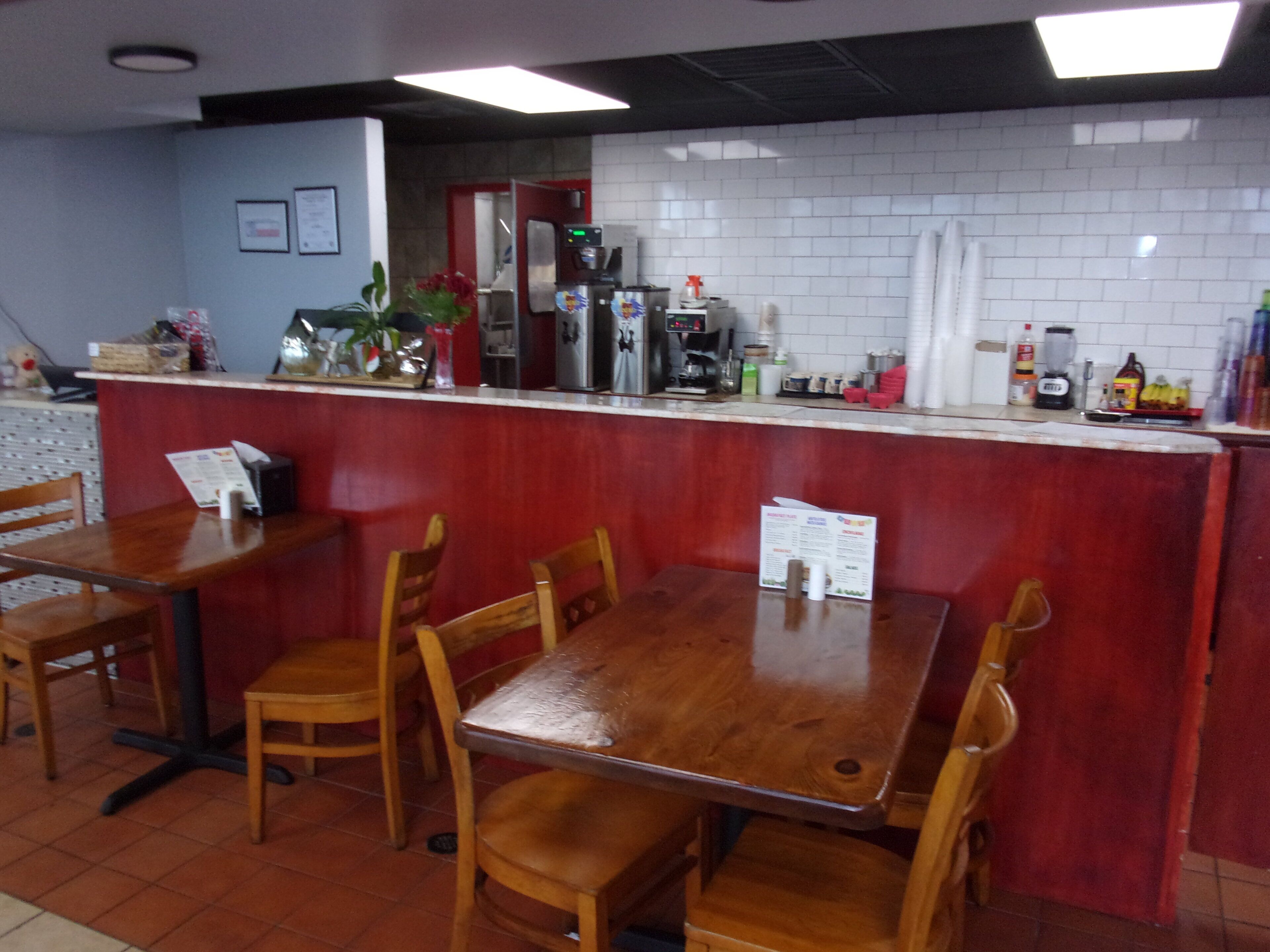 A restaurant interior with wooden tables and chairs, a counter with a menu, and a tiled backsplash.