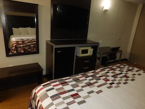 Una habitación de hotel con cama, escritorio, silla, televisor y microondas.