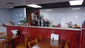 Interior de restaurante con mesas y sillas de madera, una barra con menú y un revoque de azulejos.