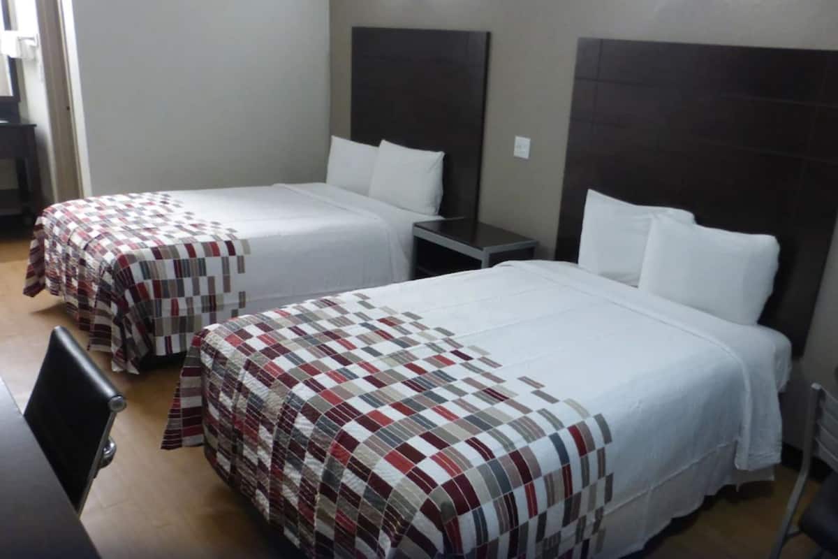 Une chambre d’hôtel avec deux lits, chacun recouvert d’une couvre-lit à motifs différents. La chambre contient également une petite table et une chaise.