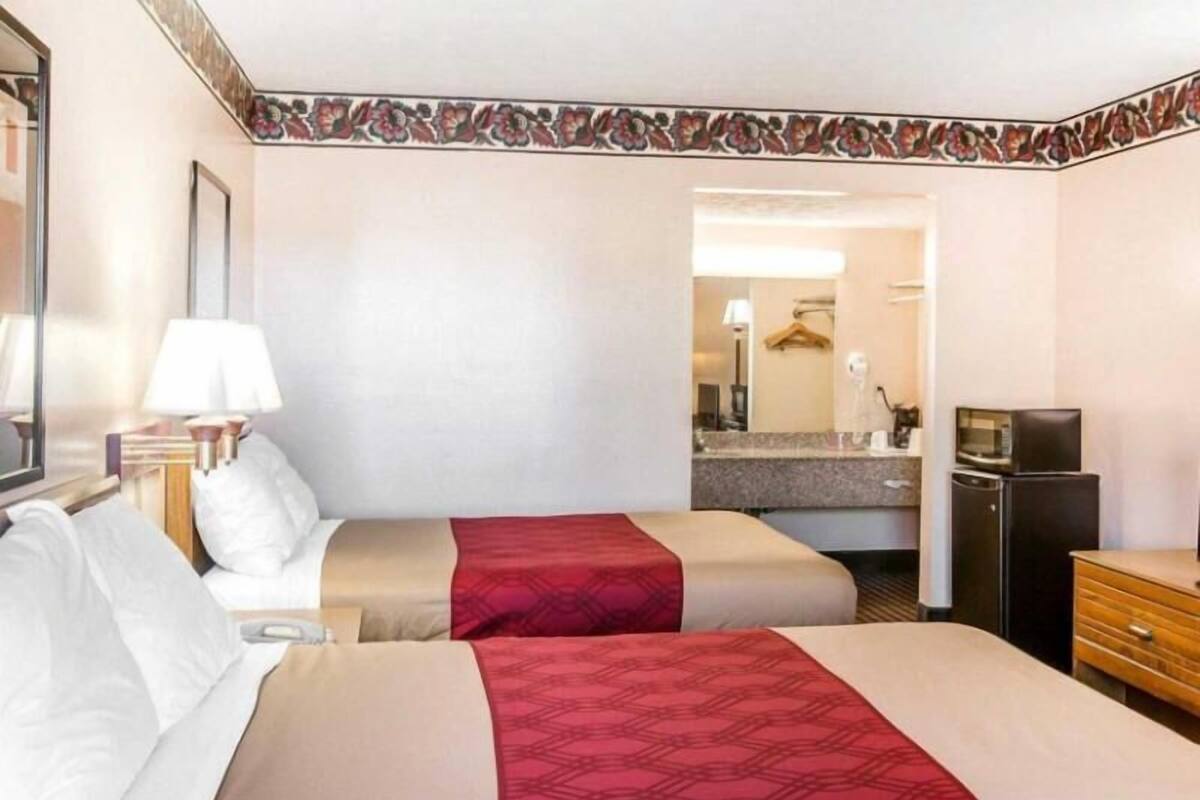 A hotel room with two beds, a desk, a refrigerator, and a bathroom visible through an open door.