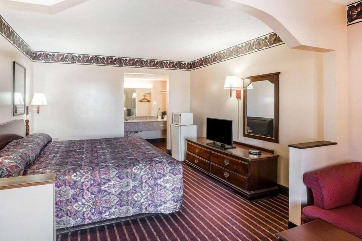 A hotel room with a bed, a dresser, a television, a mirror, and a red armchair.