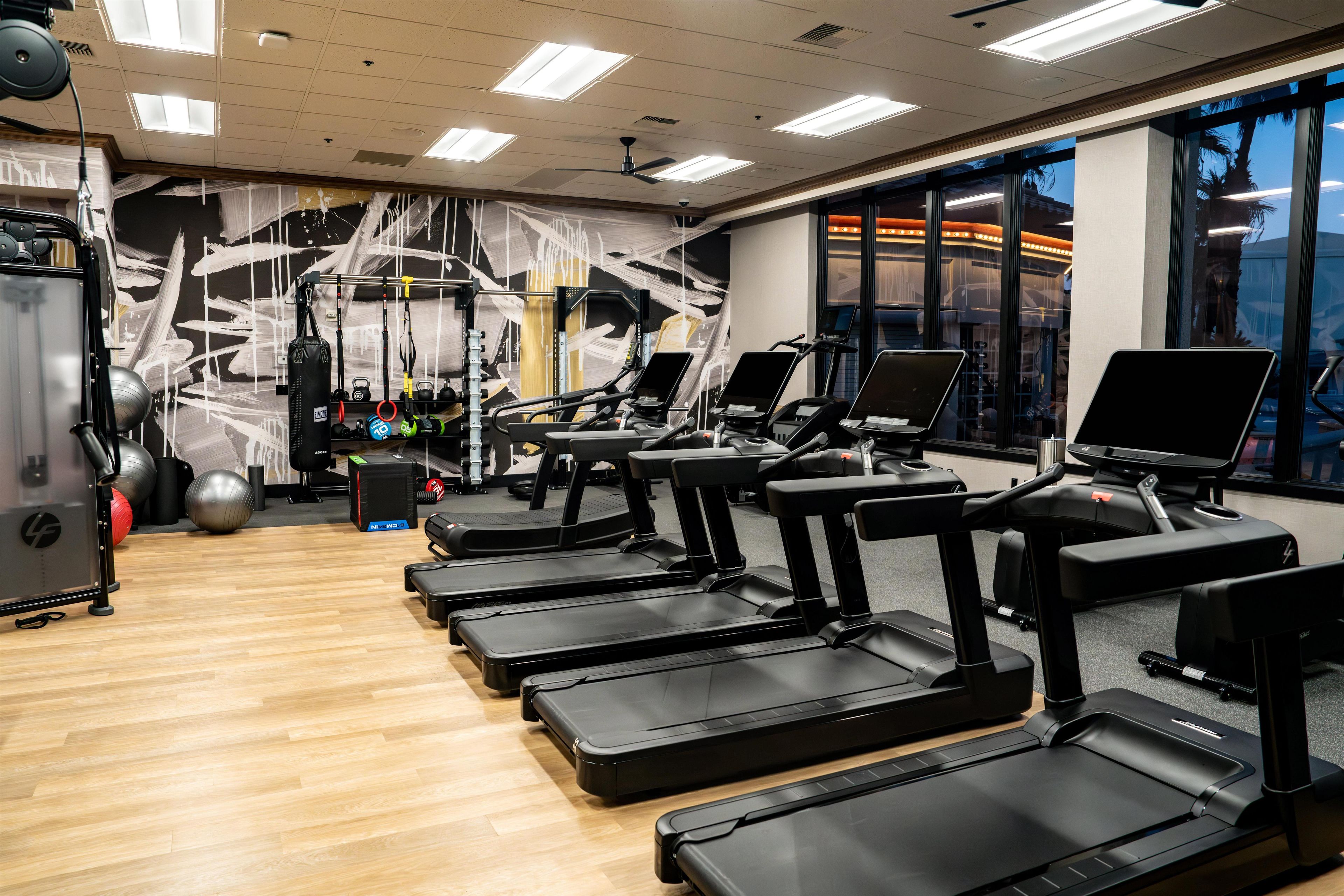 Une salle de sport équipée de tapis de course, d’appareils de musculation et de ballons d’exercice.