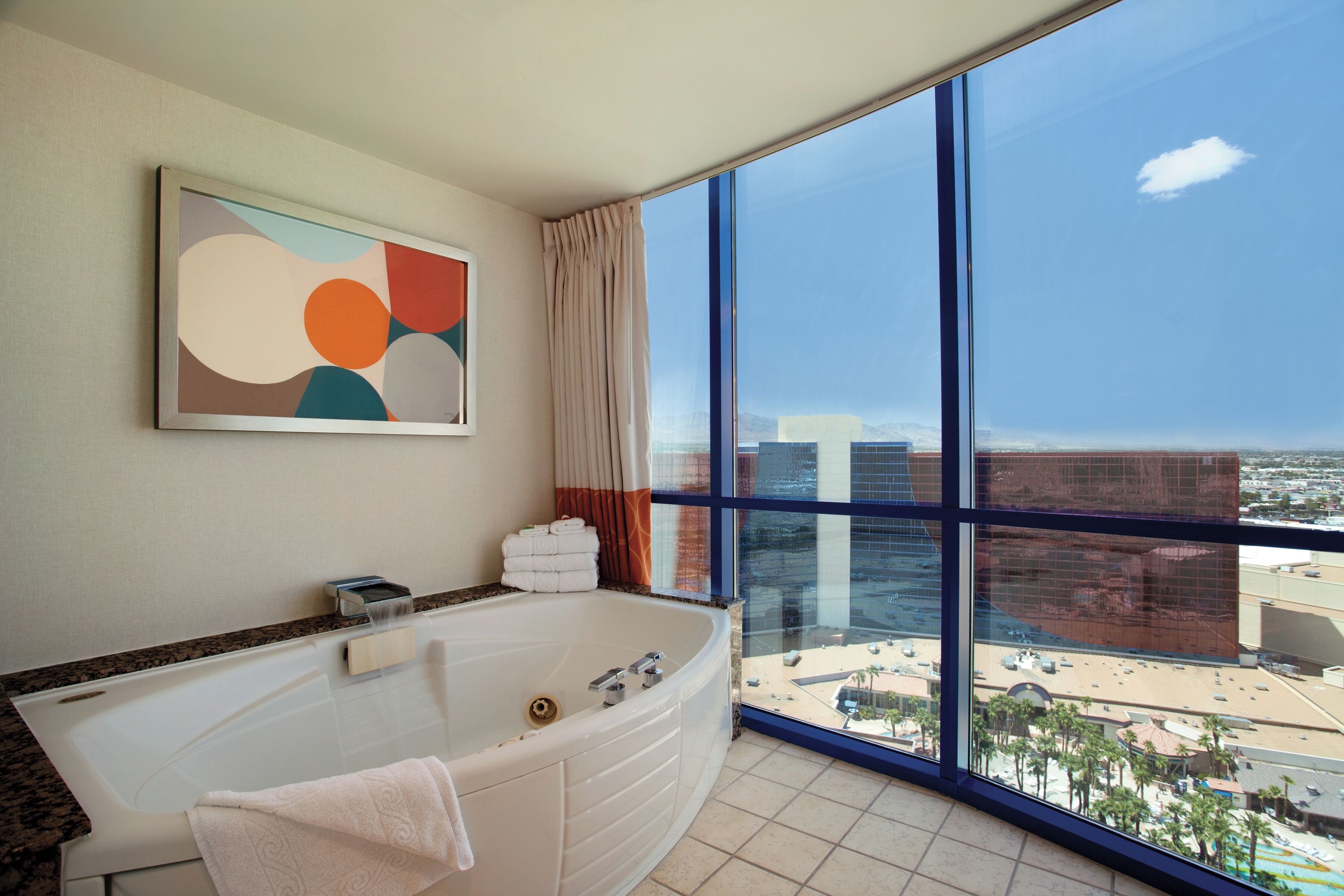 A modern bathroom with a large bathtub, a view of the city through large windows, and a contemporary abstract painting on the wall.