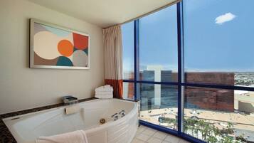 A modern bathroom with a large bathtub, a view of the city through large windows, and a contemporary abstract painting on the wall.