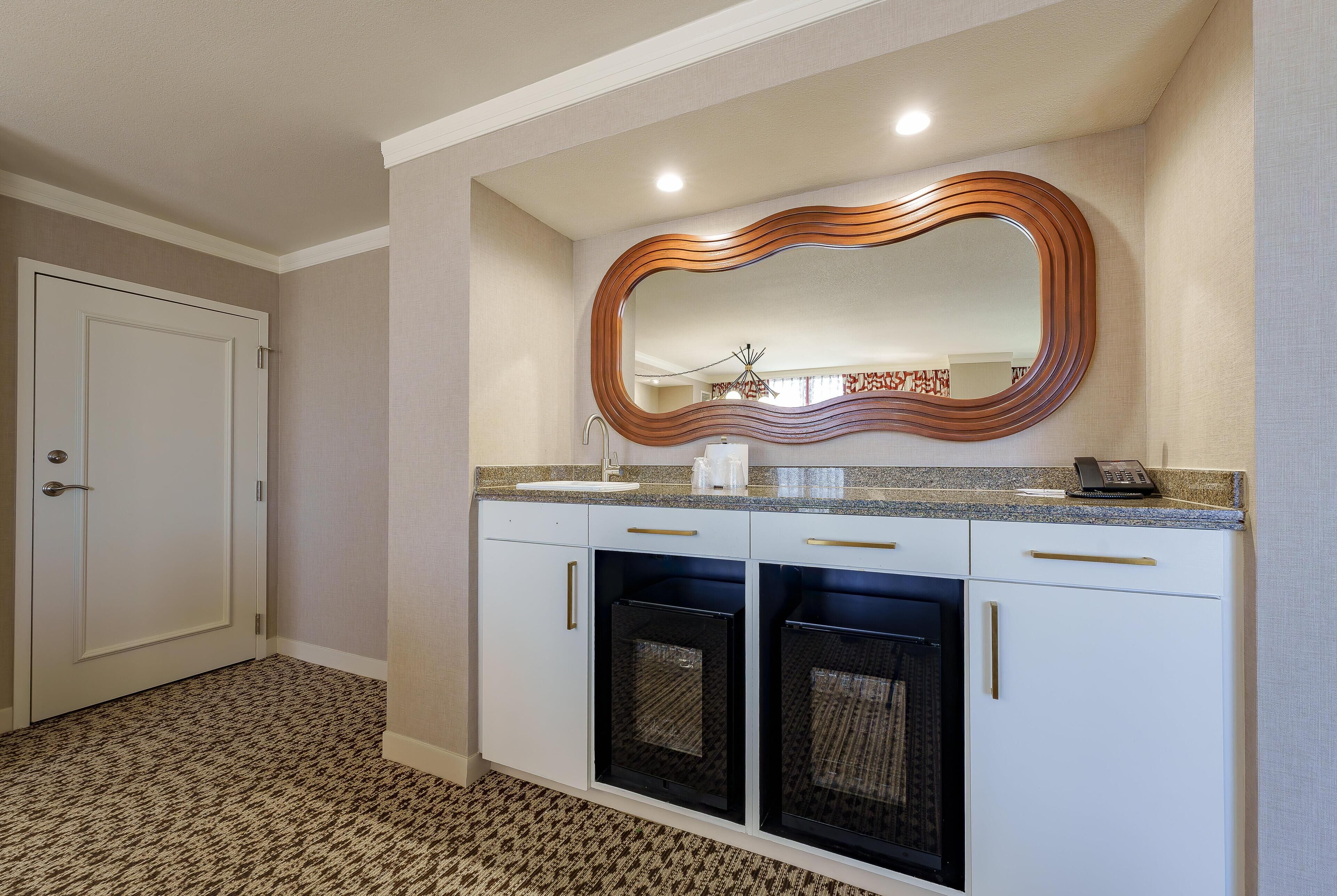 Une salle de bain avec un grand miroir, des meubles blancs, un lavabo et un espace douche.