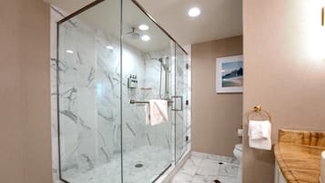 A modern bathroom with a glass-enclosed shower, marble flooring, and a wooden vanity.