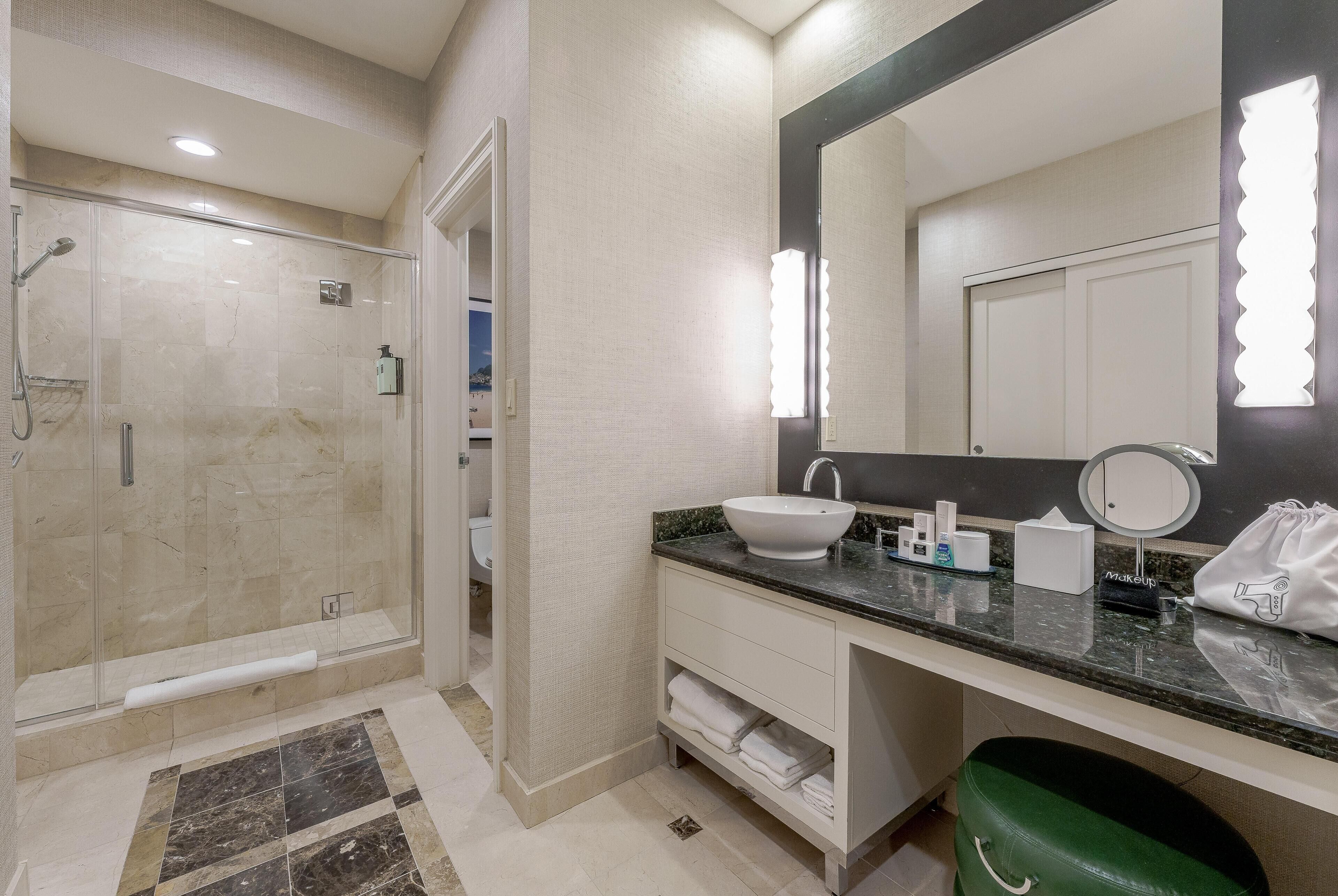 A modern bathroom with a glass-enclosed shower, a large mirror, and a vanity with a sink and toiletries.