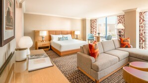 Ein Hotelzimmer mit Bett, Sofa, Schreibtisch mit Lampe und Blick auf die Stadt.