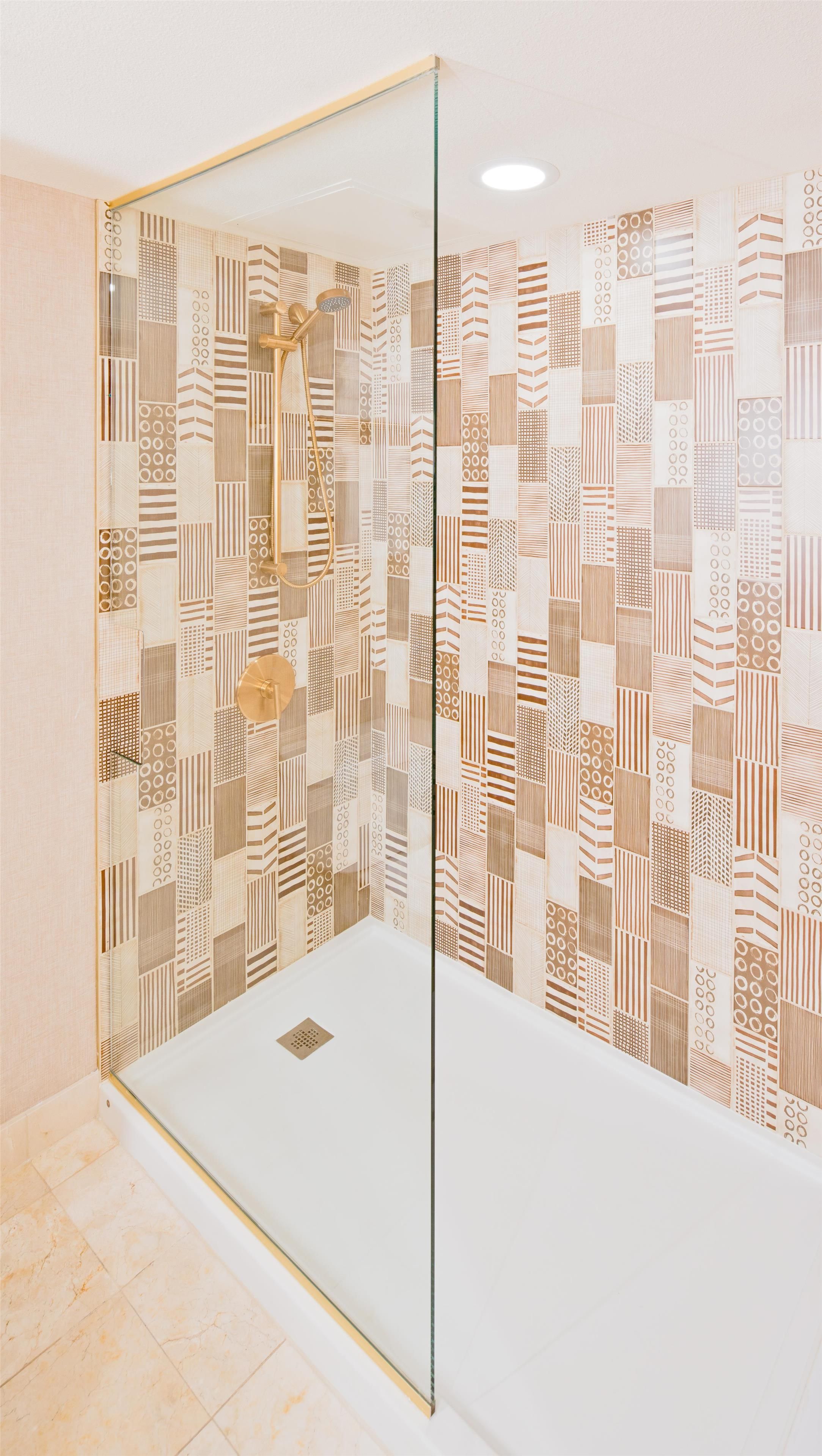A shower with a glass door and a patterned wall.