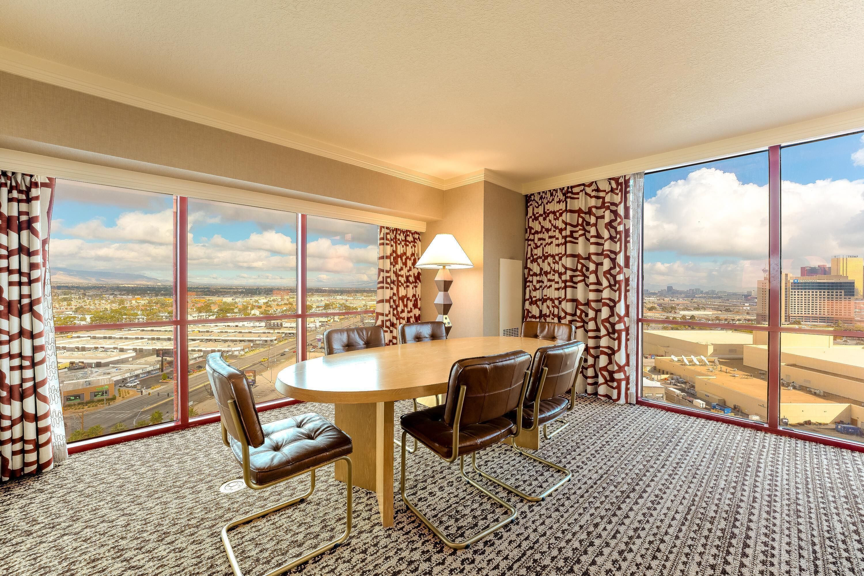A conference room with a large table, leather chairs, and a view of a cityscape through large windows.