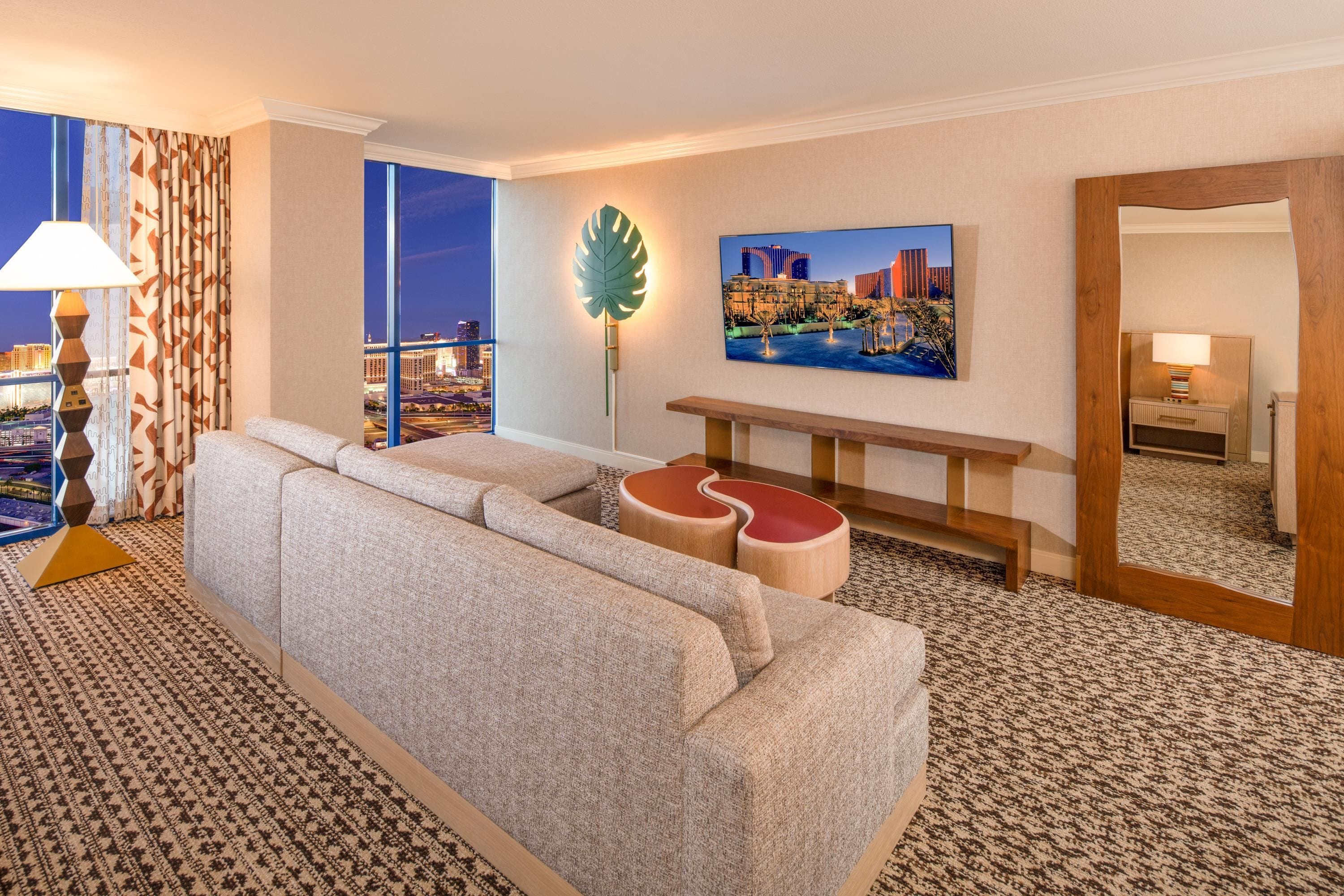 Habitación de hotel con un ventanal grande, un sofá, una mesita de café, una lámpara, un cuadro y un espejo.