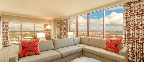 A modern living room with a sectional sofa, a coffee table, and large windows offering a city view.