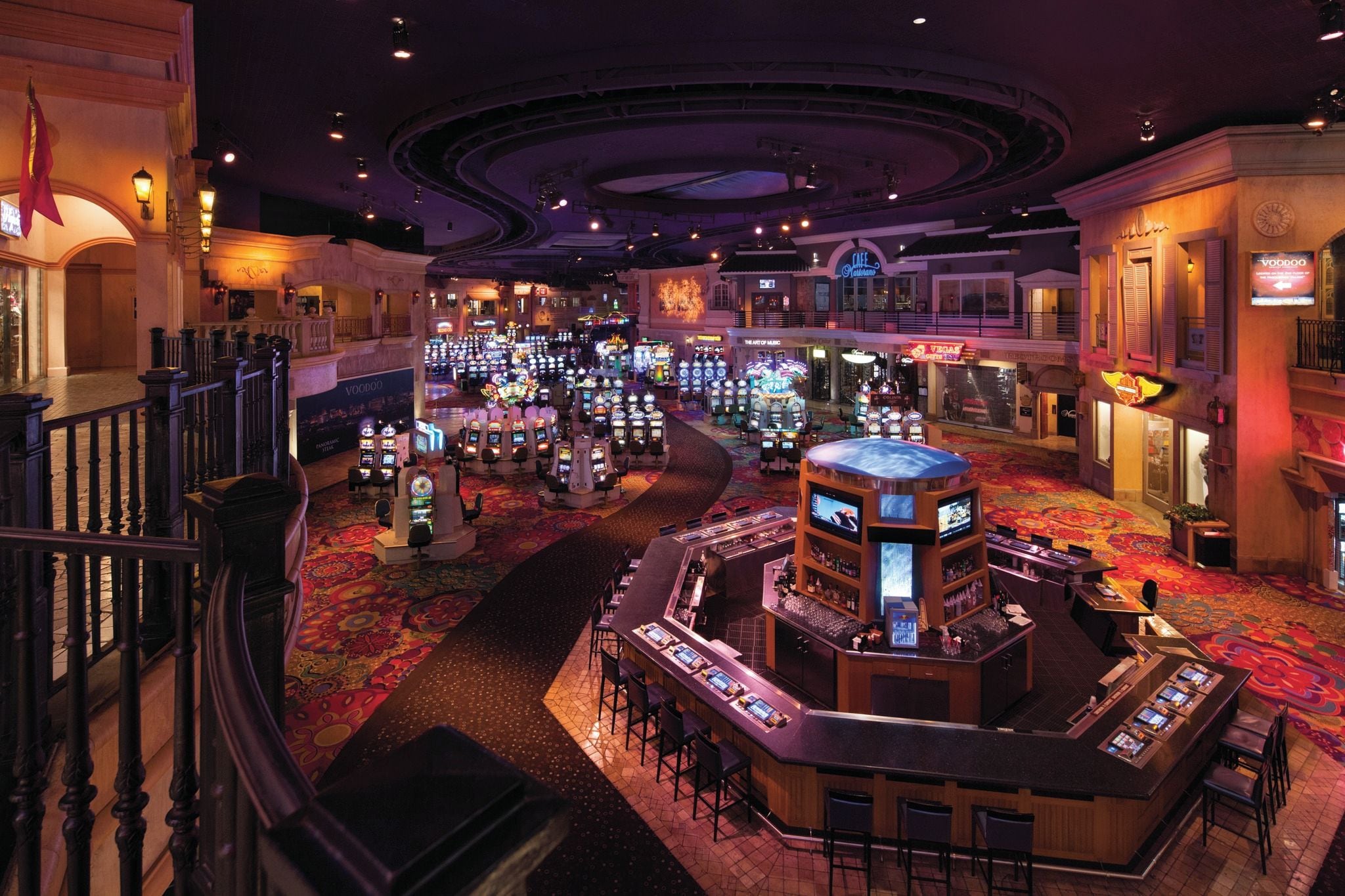 A casino floor with slot machines, a bar area, and a staircase leading to upper levels.