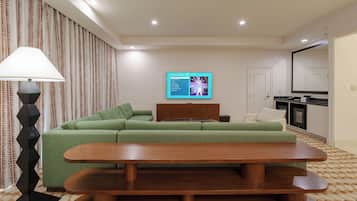 A modern living room with a green sectional sofa, a wooden coffee table, a lamp, and a wall-mounted TV displaying a presentation.