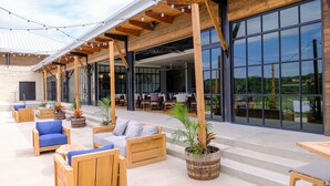 Ein Sitzbereich im Freien mit Holzmöbeln und Topfpflanzen, großen Fenstern und einer überdachten Terrasse.