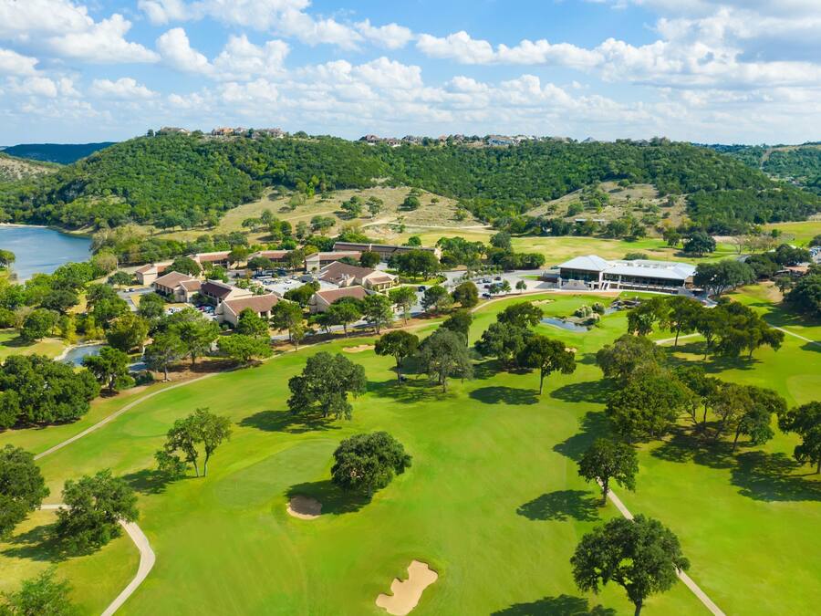 Vista aérea de un campo de golf con club, zona residencial y un lago al fondo.