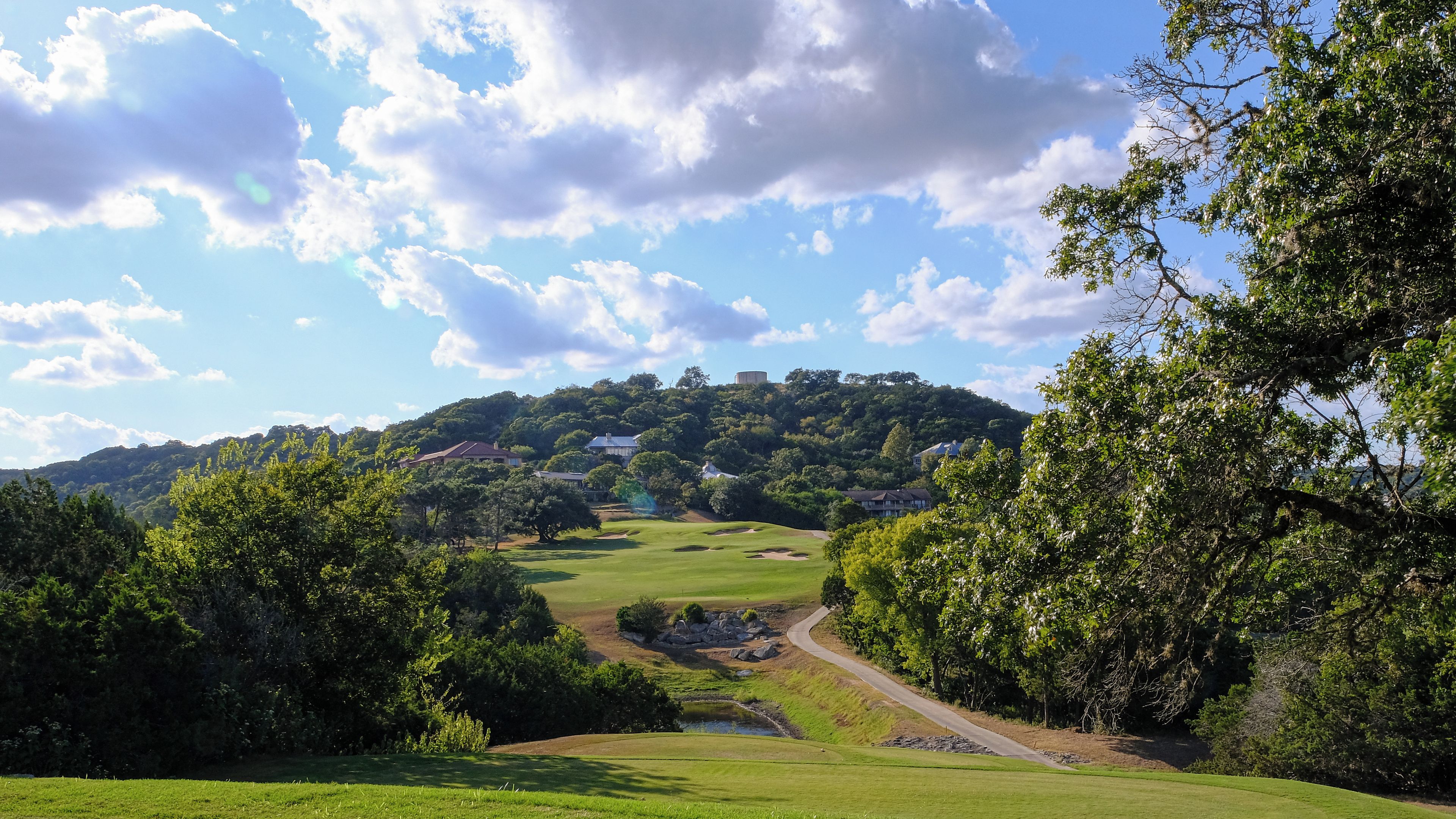 Un campo de golf con un sendero sinuoso, abundante vegetación y casas al fondo.