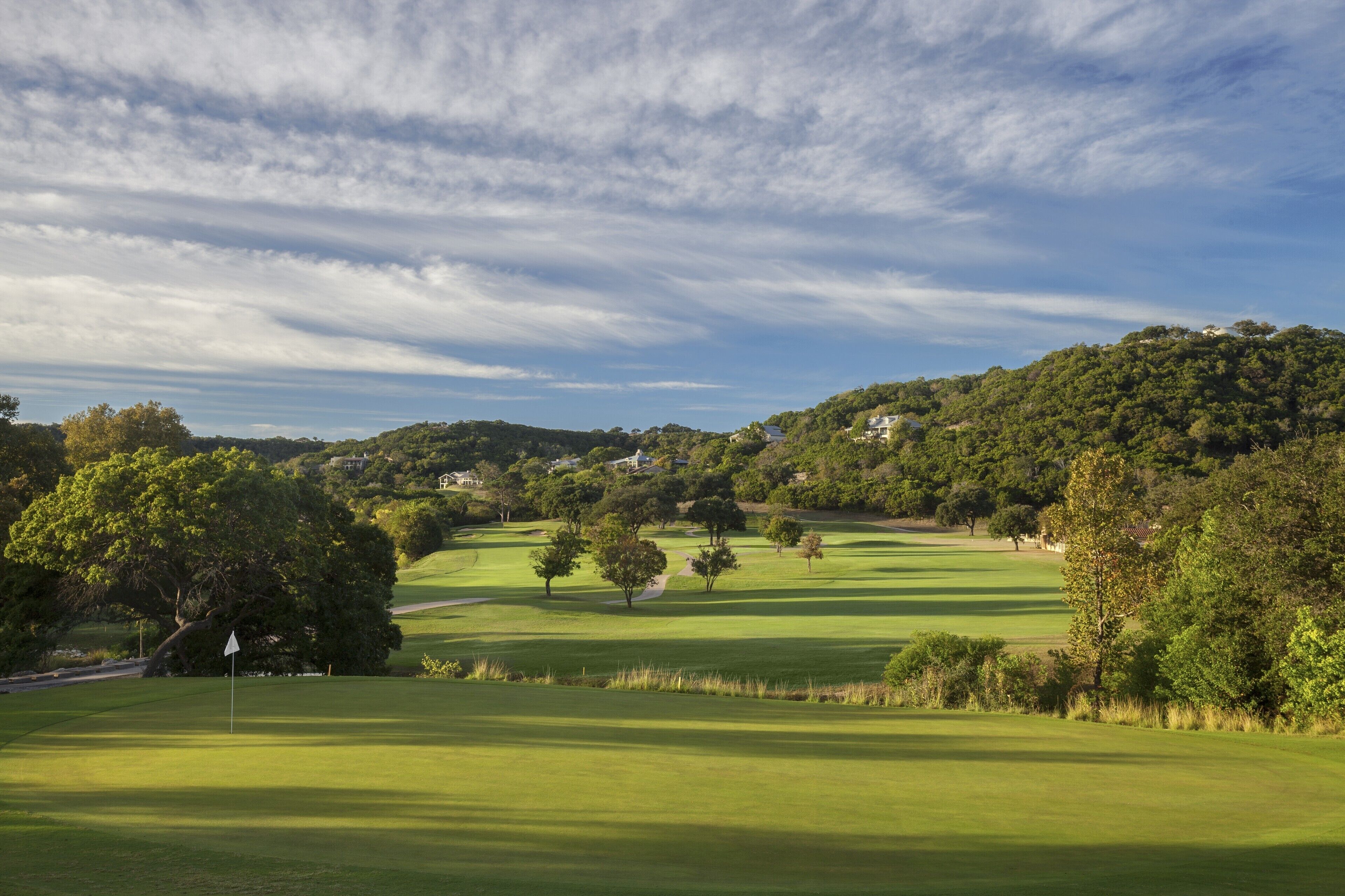 Un campo da golf con una bandiera, alberi e una collina sullo sfondo.