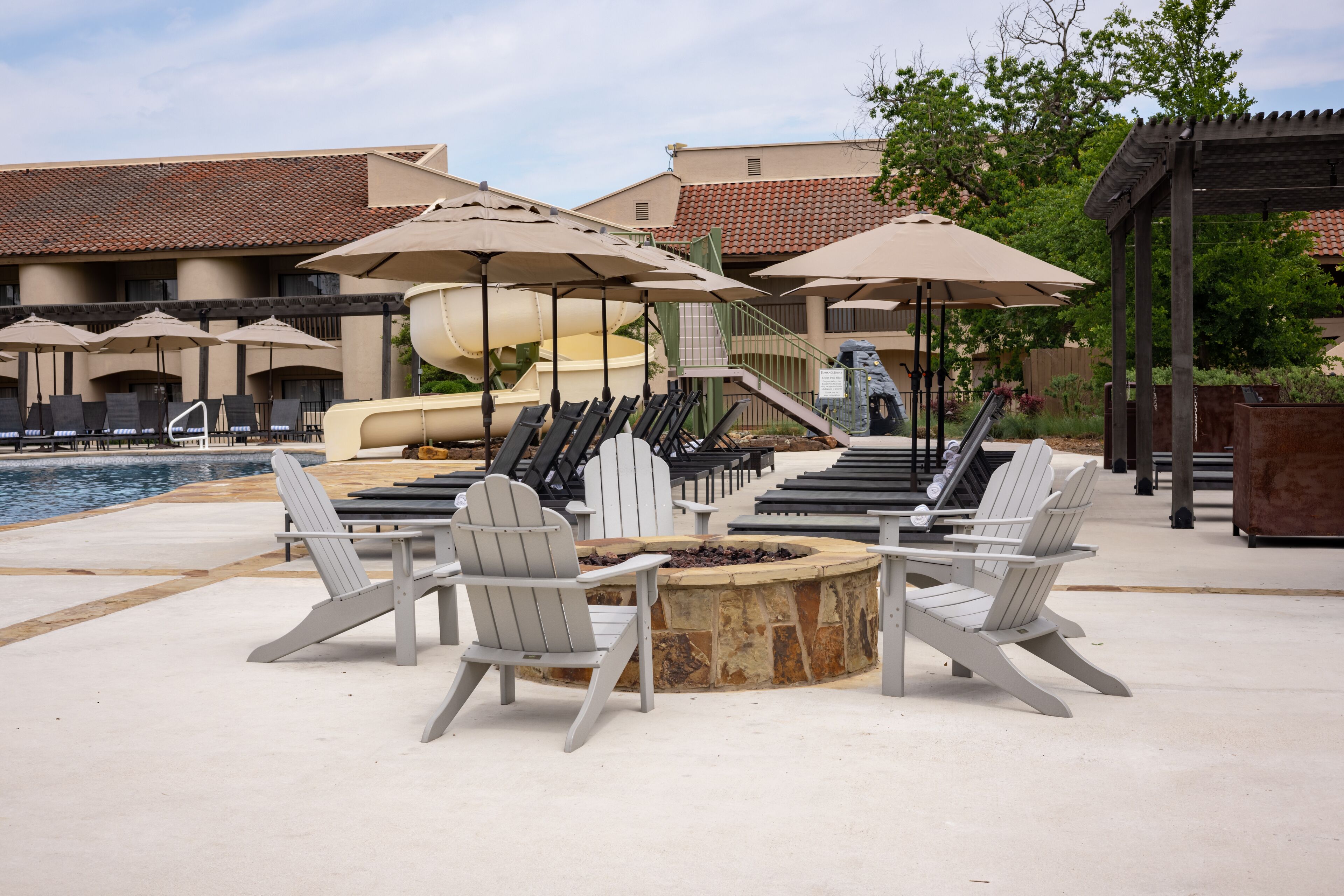 Zona junto a la piscina con sillones Adirondack, una chimenea y sombrillas.