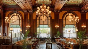 Un comedor espacioso con candelabros ornamentales, paneles de madera y ventanas amplias que ofrecen luz natural.
