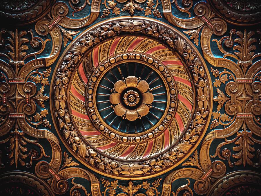 A detailed, ornate ceiling with a central circular design surrounded by intricate patterns and gold accents.