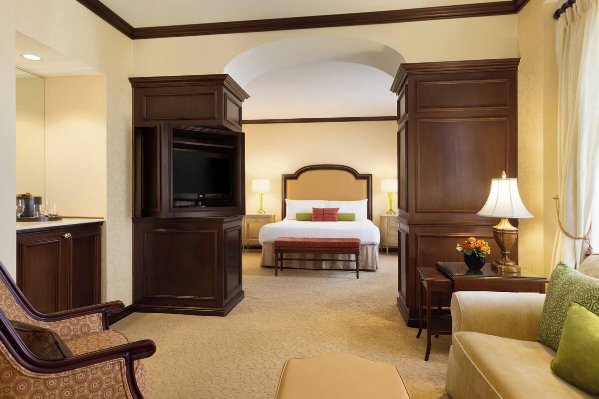 Quarto de hotel com cama, televisão, secretária, cadeira e sofá.