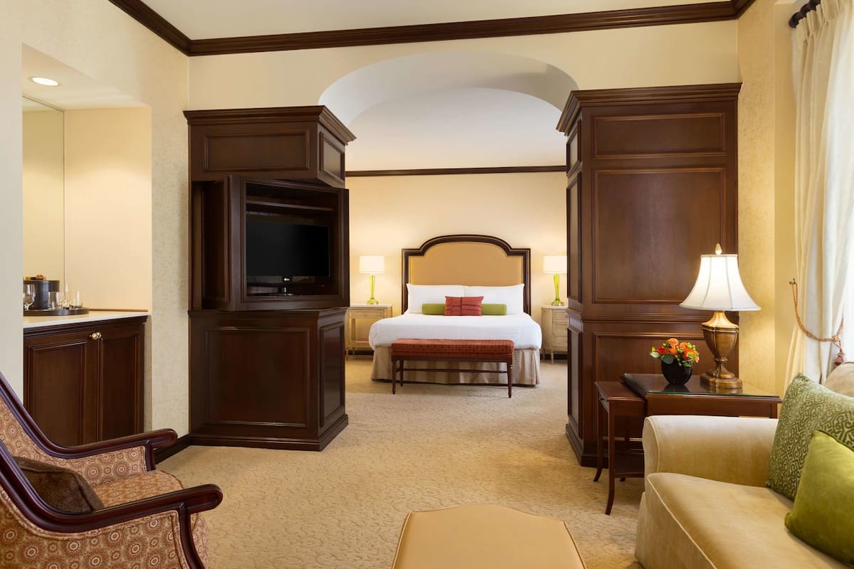 Quarto de hotel com cama, televisão, escrivaninha, cadeira e sofá.