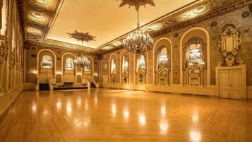 A spacious ballroom with ornate chandeliers, arched doorways, and detailed wall decorations.