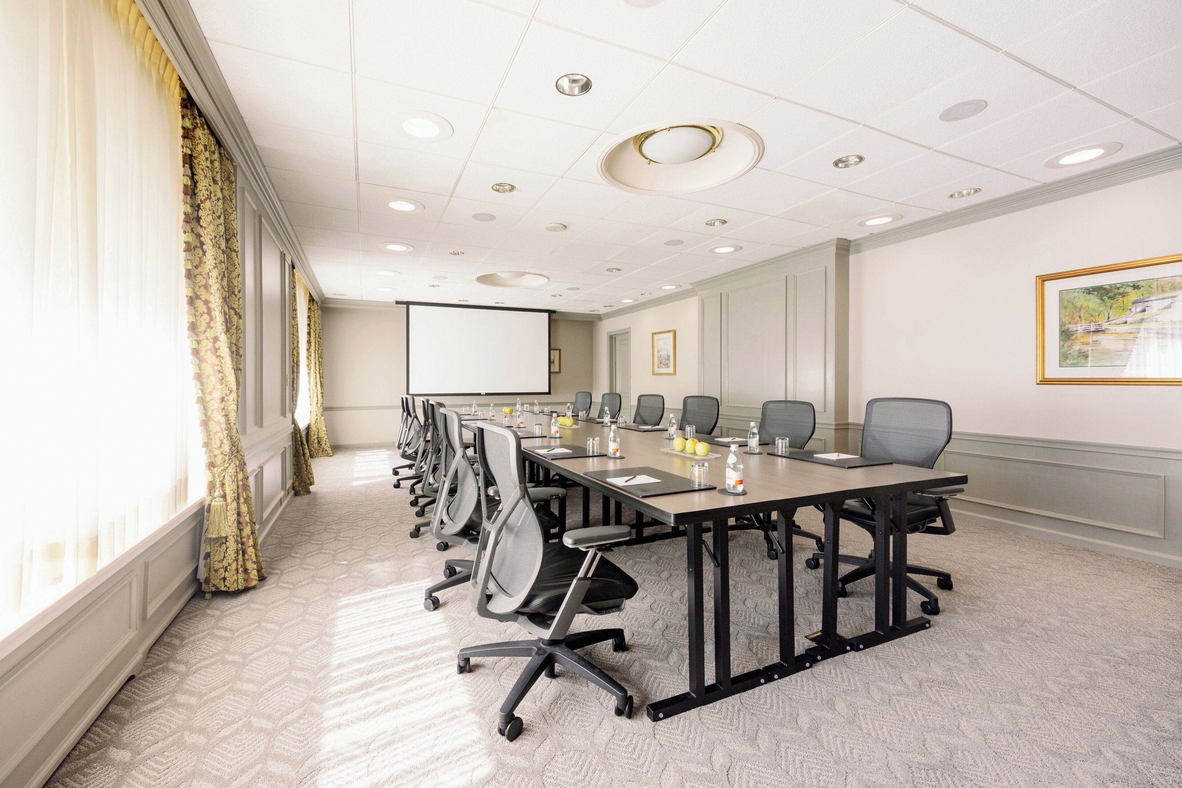 A conference room with a long table, chairs, a projector screen, and a carpeted floor.