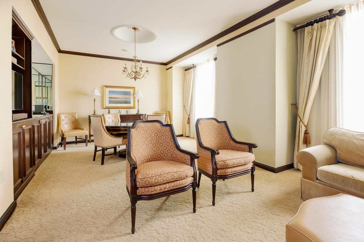 Um quarto amplo com uma janela grande, um candelabro e uma área de jantar com mesa e cadeiras.