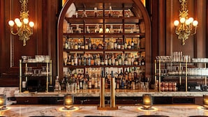 Un área de bar con mostrador de mármol, varias estanterías llenas de botellas de licor y dos candelabros.