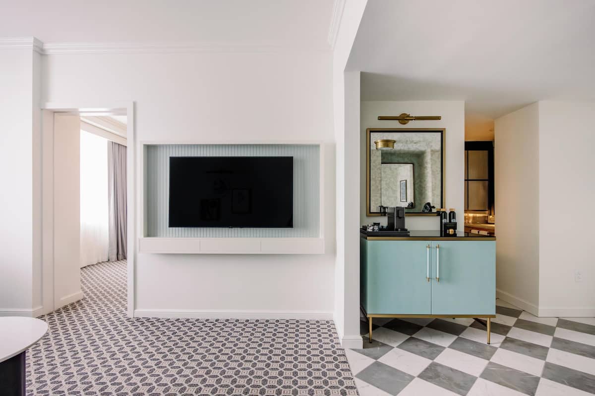 Quarto de hotel com televisão de tela plana na parede, um armário azul-claro com puxadores dourados e um padrão de piso quadriculado.