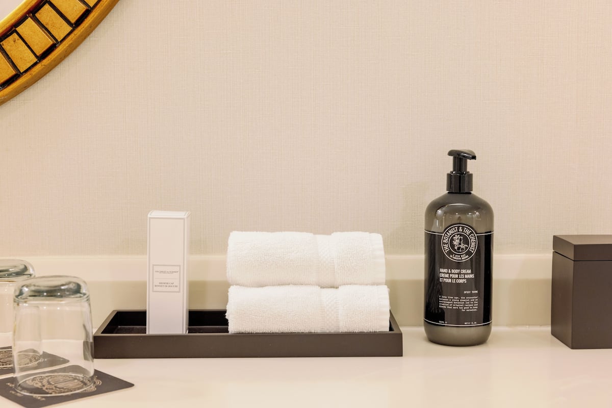 Casa de banho com banheira, um frasco de creme para as mãos e corpo, duas toalhas enroladas e um dispensador de sabonete.